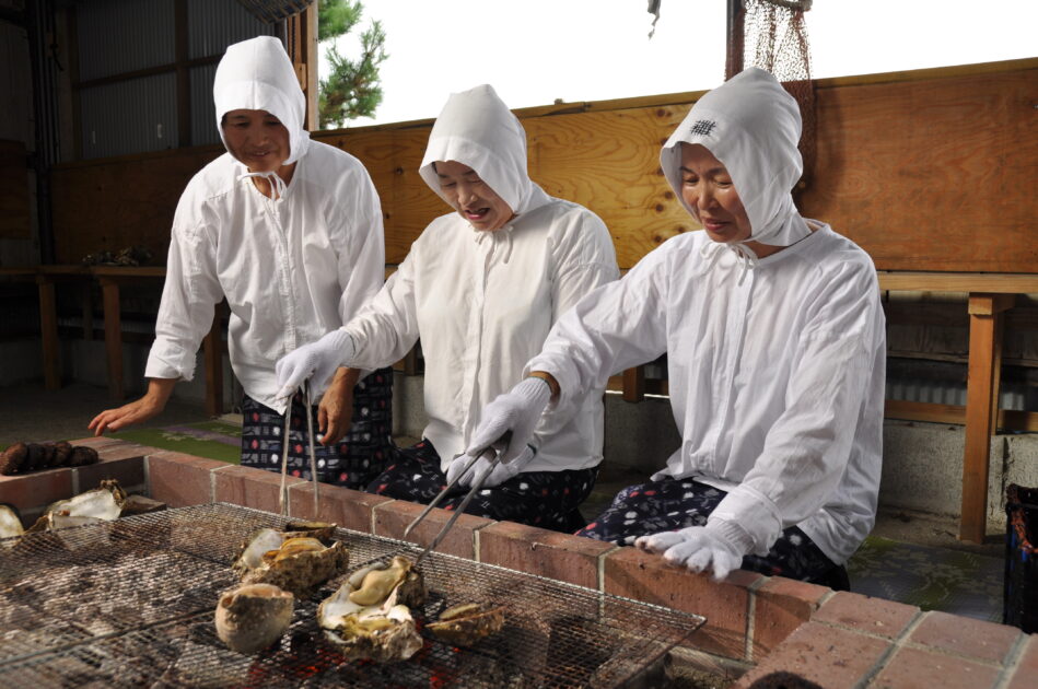 Ama woman grilling fresh seafood over charcoal fire in traditional hut